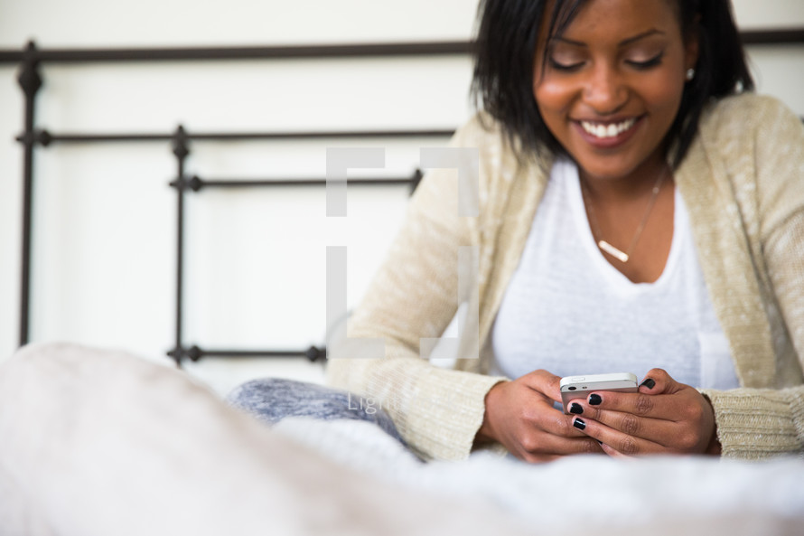 young woman sitting in bed texting