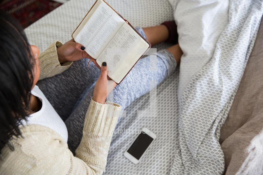 young woman sitting in bed reading a Bible