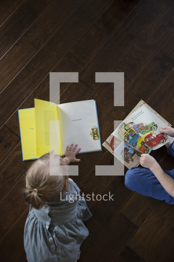  a toddler boy and girl reading a book on the floor 