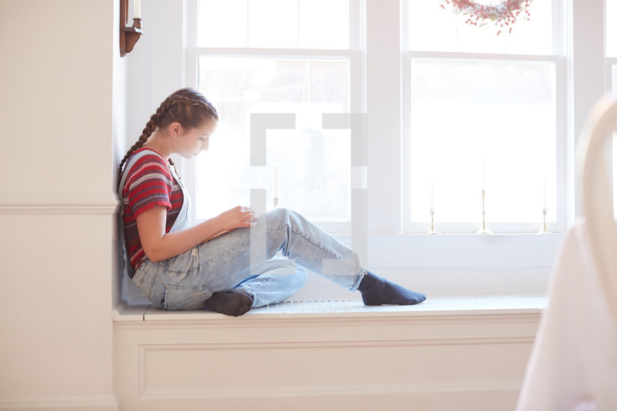 a girl sitting in a window reading a book 