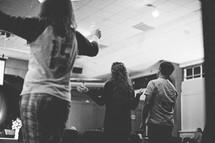 young people inspired and standing up with raised hands at a worship service 