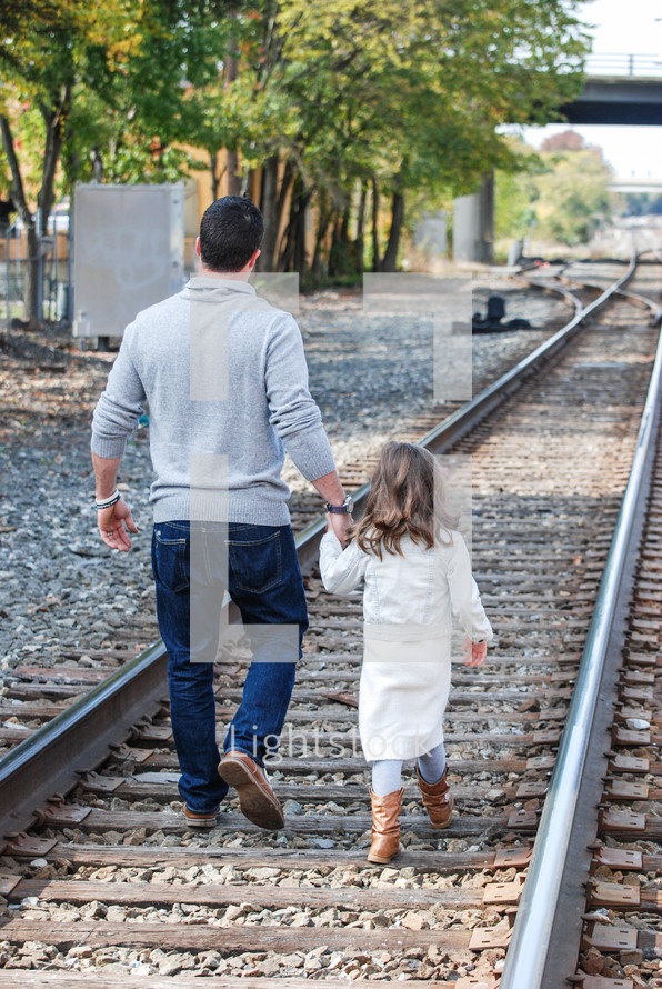 a father and daughter walking on train tracks 