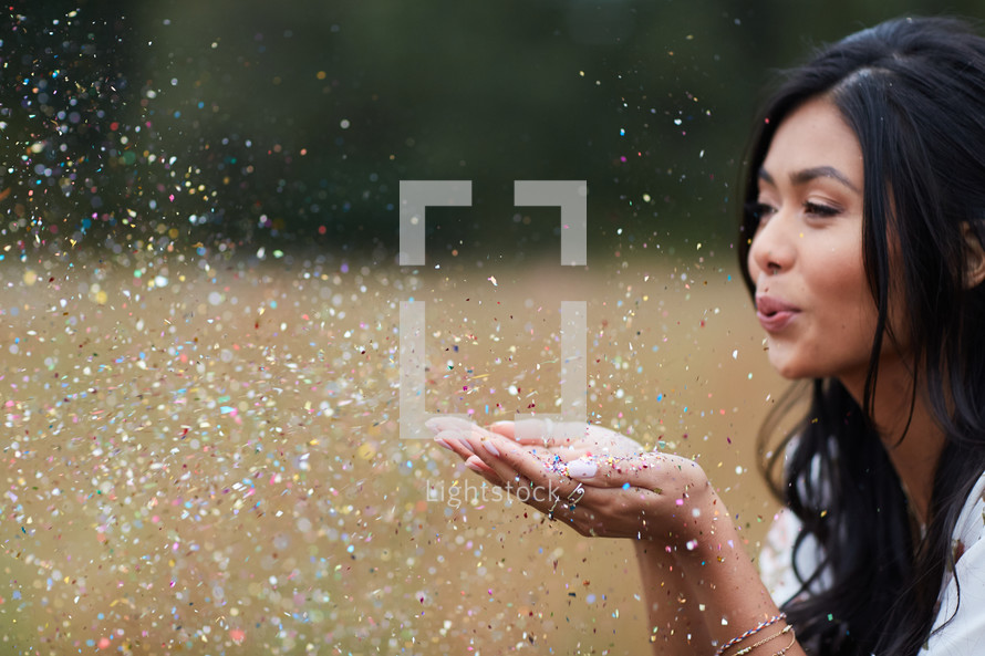 young woman blowing confetti out of her hands in a field 