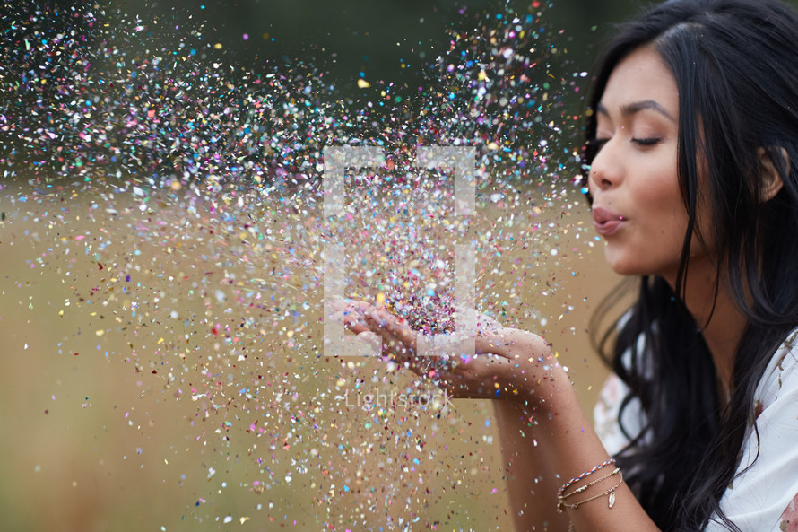 young woman blowing confetti in a field 