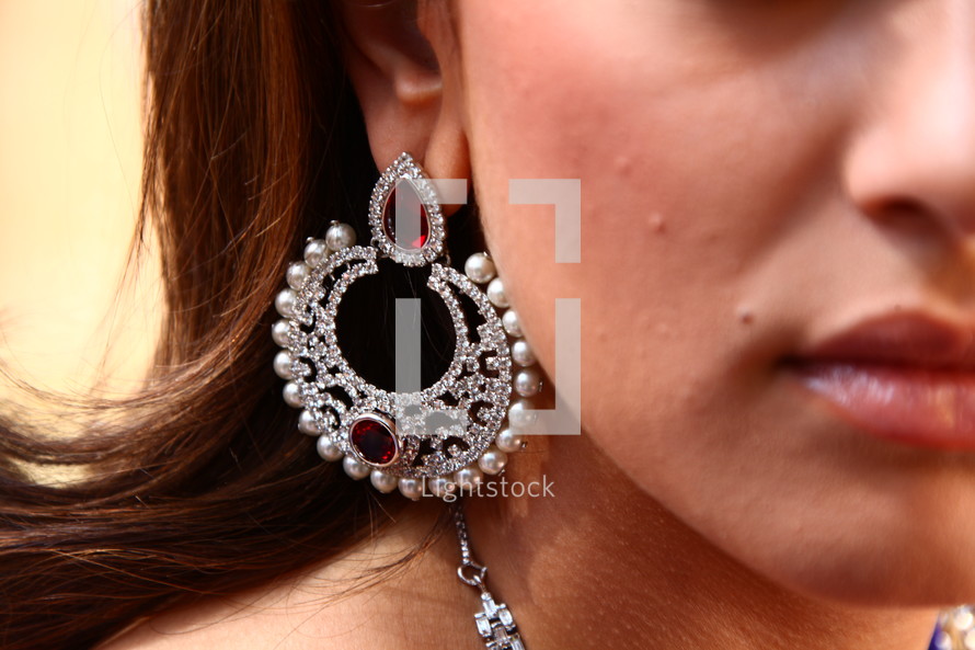 A woman wearing a very large earring with gemstones and pearls.