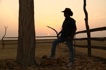 man in a cowboy hat standing by a fence in a desert 