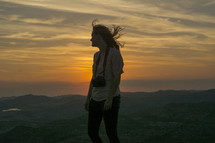 woman with a camera standing on a mountain top at sunset