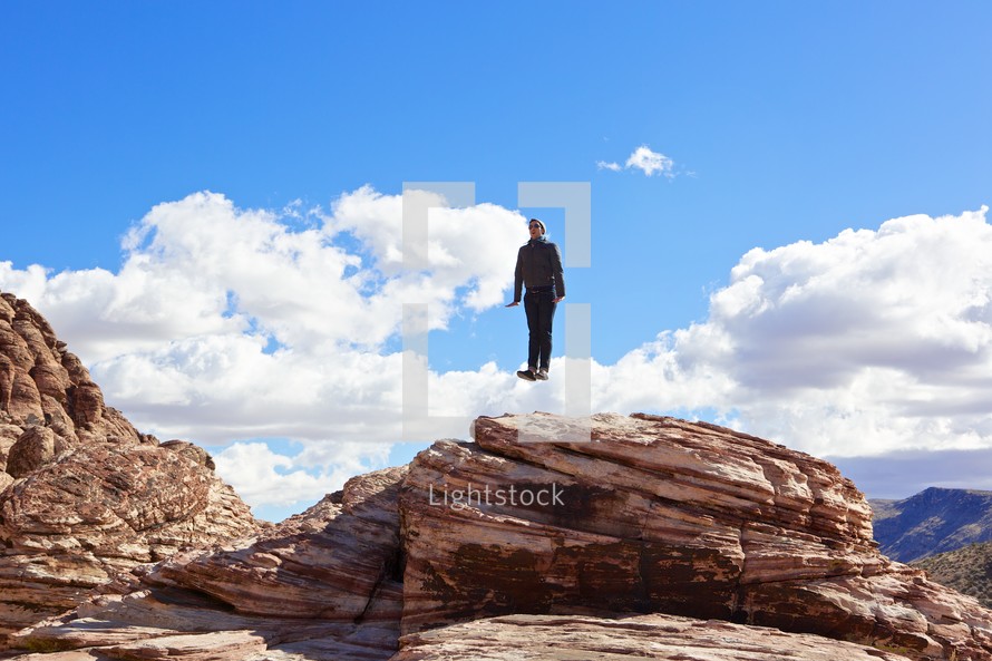 man jumping on top of a red rock