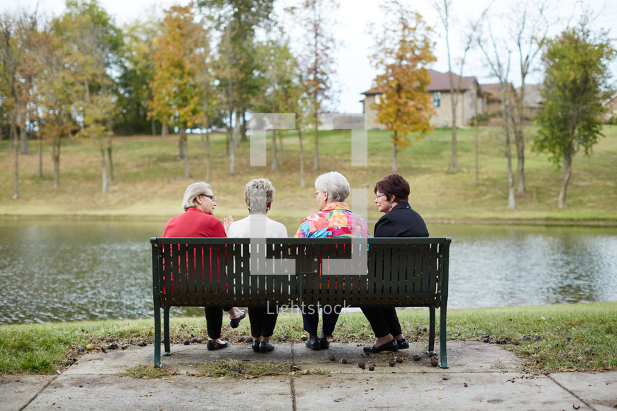 elderly women sitting on a park bench talking 