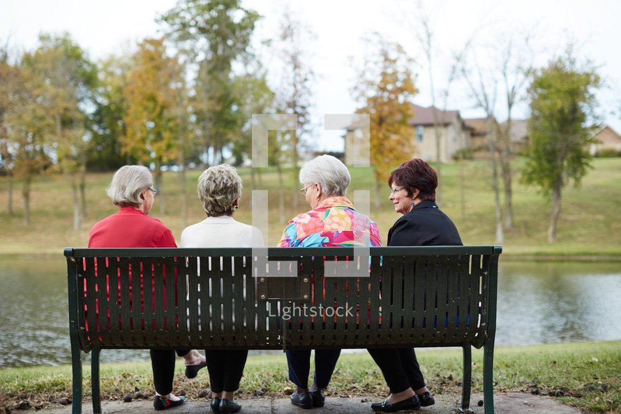elderly women talking sitting on a bench outdoors 