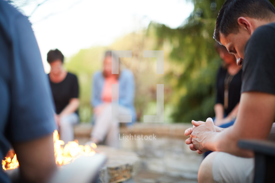 friends sitting around a fire pit praying