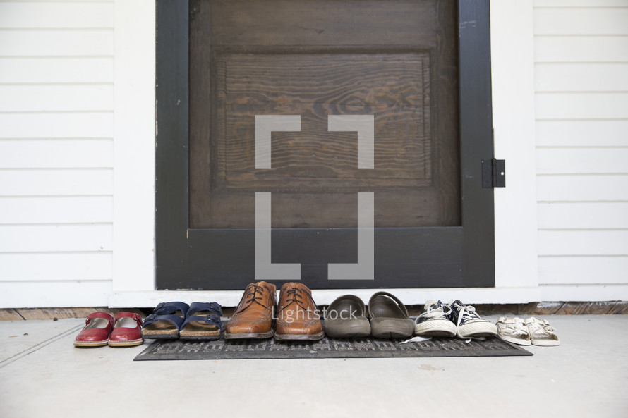 row of a families shoes on a mat in front of a door 