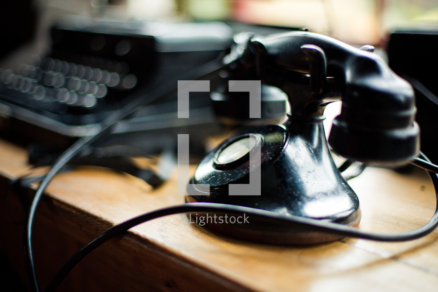 Old school telephone and typewriter on a wooden desk.