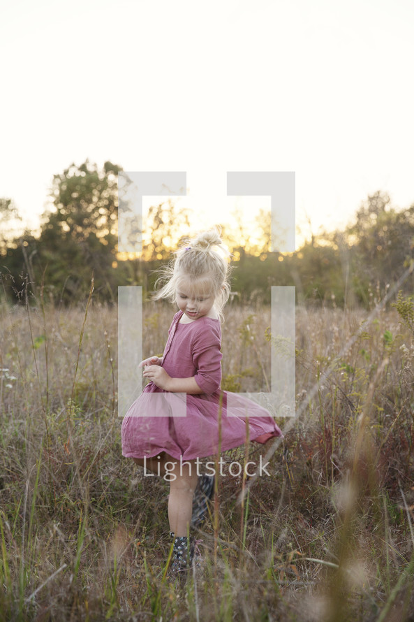 a toddler girl twirling her dress in tall grasses 