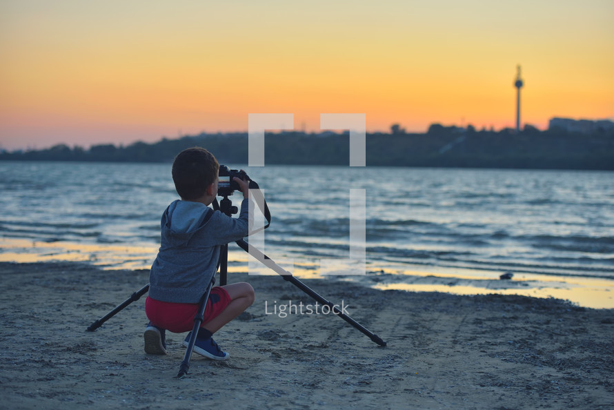 child filming the sunset on a beach 