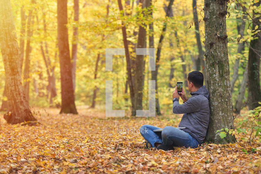 Man taking pictures with smartphone in forest, autumn colors