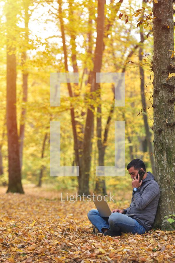 Man with laptop and smartphone in forest, autumn colors, sunset warm light