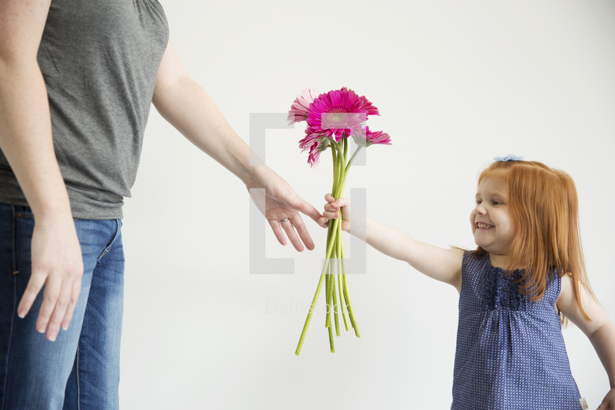 A little girl hands her mother a bouquet of pink flowers.