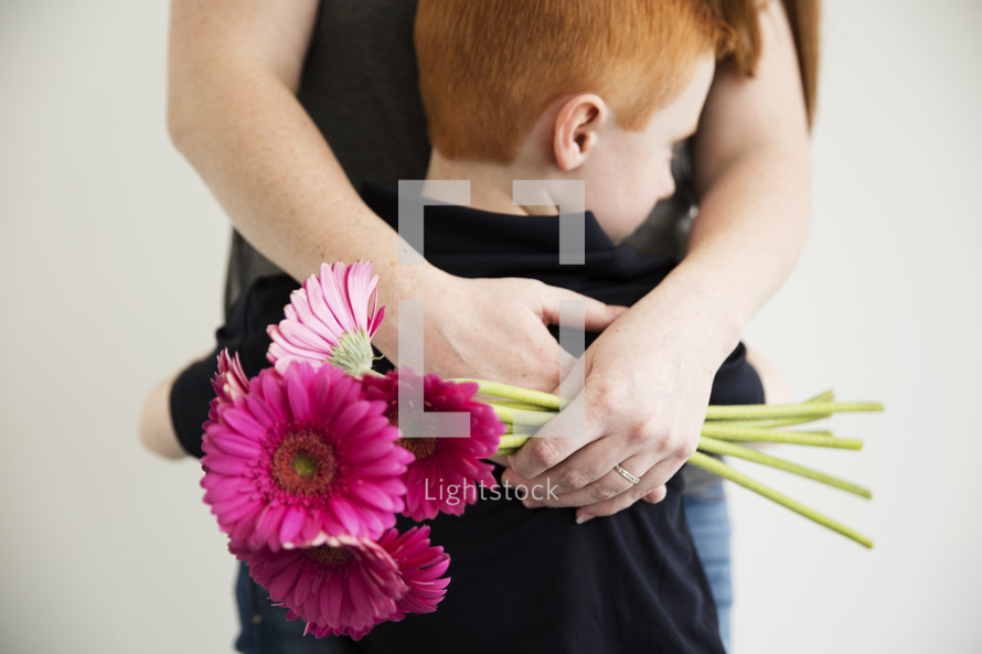 A mother hugs her young son and holds a bouquet of flowers.