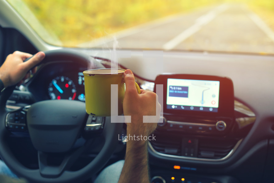 Male driver drinking hot coffee while driving on road in autumn warm colors