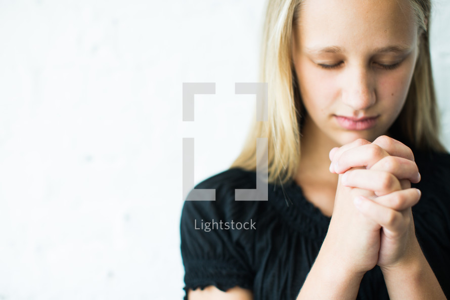 teen girl with head bowed and praying hands 