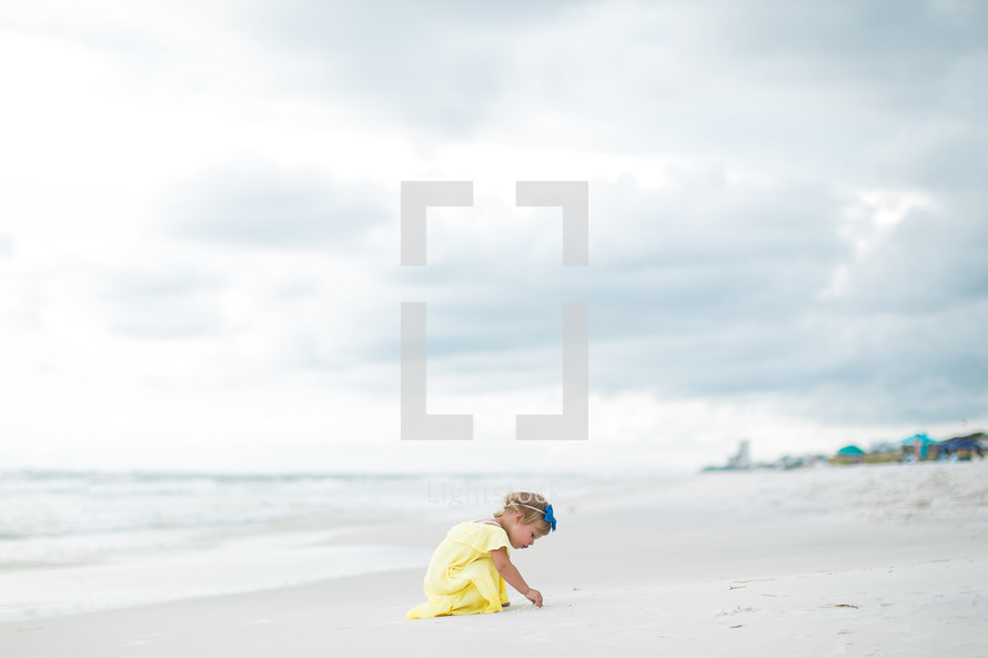 a toddler girl playing in sand on the beach 