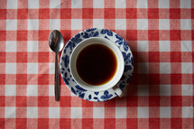 coffee cup and saucer on a red checkered tablecloth