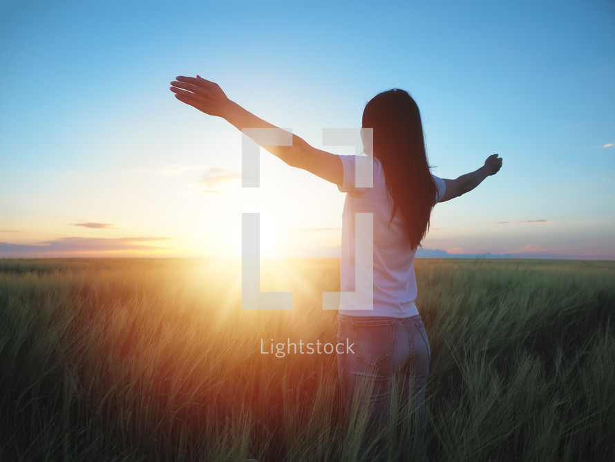 woman standing in a field with outstretched arms 