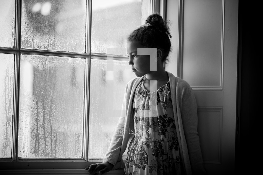 a girl sitting in a window watching the rain 