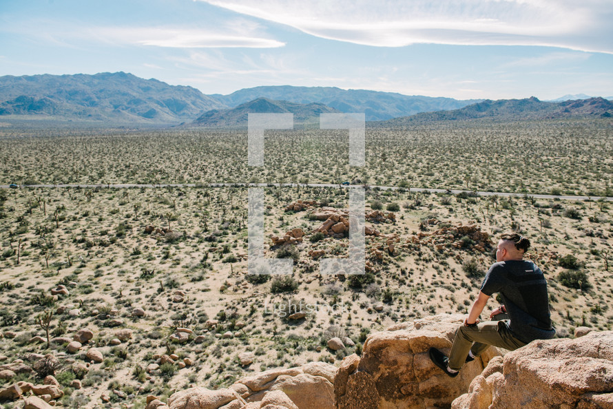 a man sitting on a rock looking out at a desert landscape 