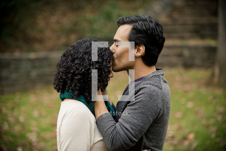Man kissing woman on the head as they stand in a park.