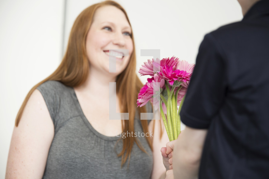 A mother receives a bouquet of pink flowers from her young son.