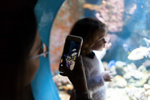 Young woman with child watch a fish in aquarium. Silhouettes of people visiting the large aquarium in Livorno, Italy.