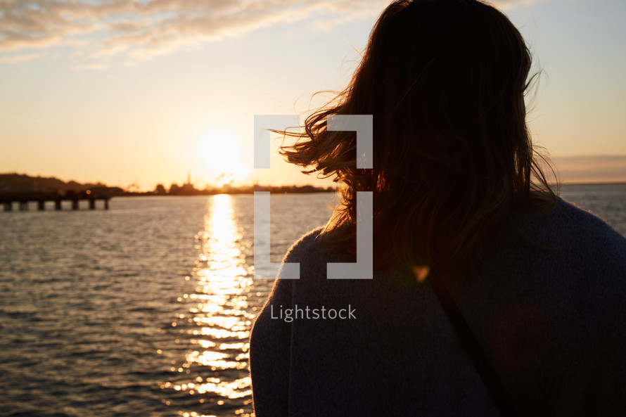 a woman looking out at water at sunset 