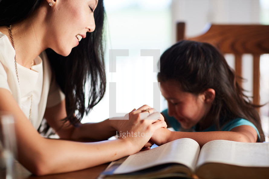 mother and daughter reading the Bible and praying together at the kitchen table 