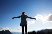 a woman with outstretched arms standing and taking in a mountain view 