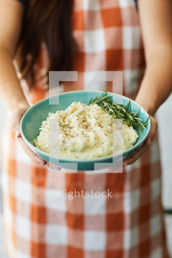 a woman holding a bowl of mashed potatoes 