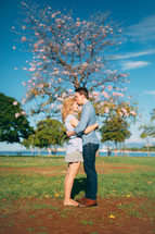 Embraced couple outside by a tree.