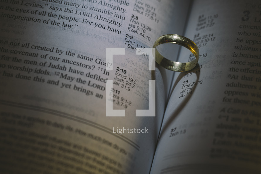 a wedding band on the pages of a Bible with heart shadow 