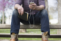 a man listening to a podcast outdoors holding a Bible 