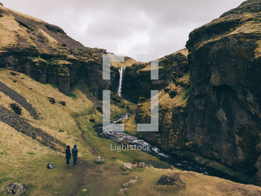 couple watching a waterfall on a green mountain 