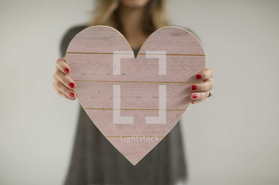 a woman holding out a wooden pink heart 