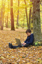 boy with laptop in forest, autumn colors, sunset warm light