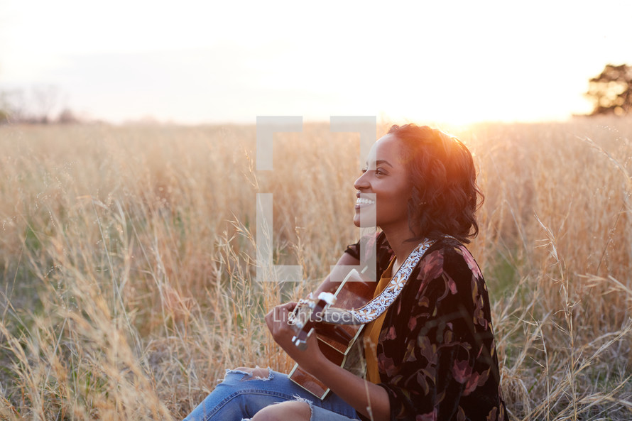a woman sitting in a field with a guitar 