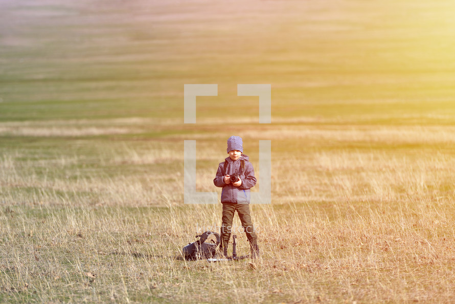 boy with a camera standing in a field 