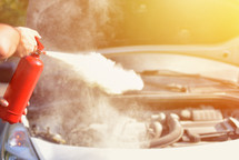 man demonstrating how to use a fire extinguisher over a car engine