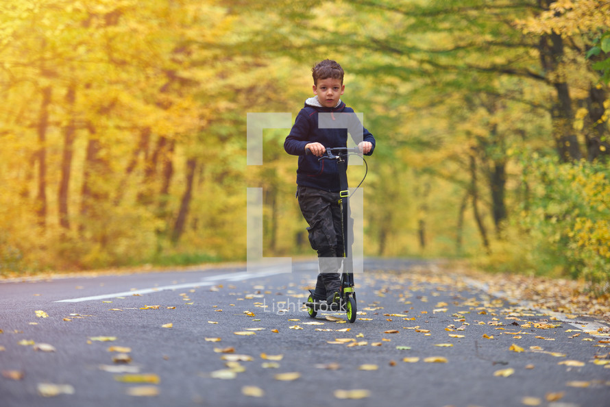 boy riding scooter, outdoors in autumn environment on sunset warm light