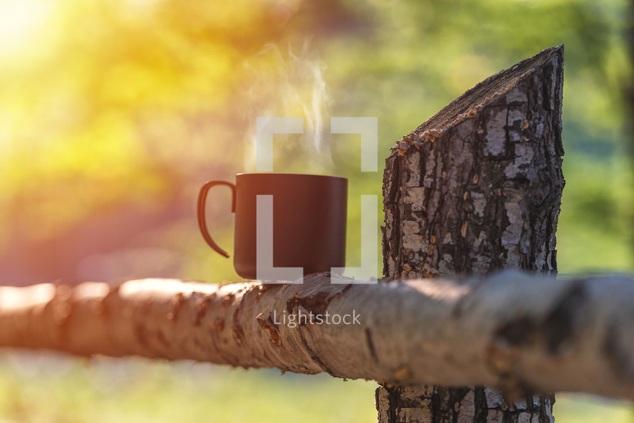 Cup with coffee on wood fence over mountain forrest landscape with sunlight. Beauty nature background