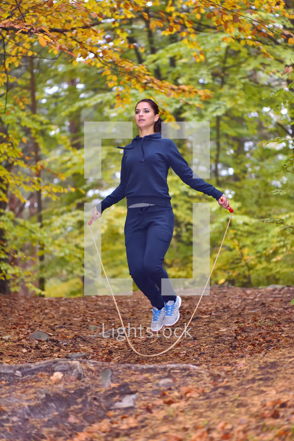 Sporty young woman jumping rope in park with autumn colors background