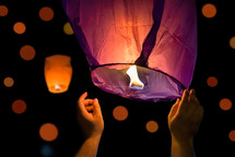Hands of tourist launching sky lantern to the sky. Lampions in the dark